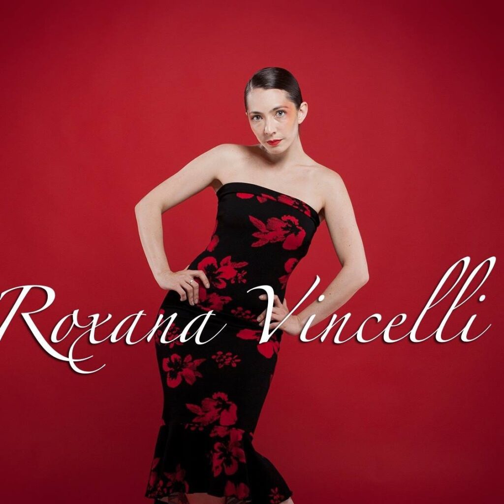 Model poses in elegant black and red floral dress against red backdrop.