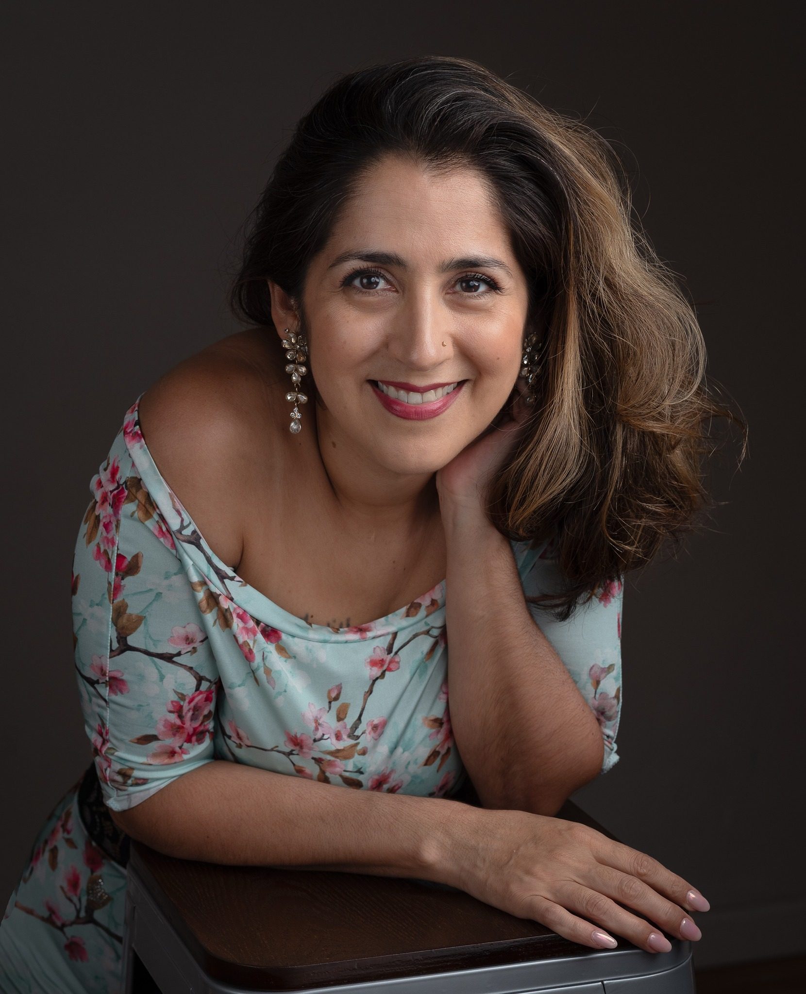 A smiling woman with wavy hair poses against a dark background.