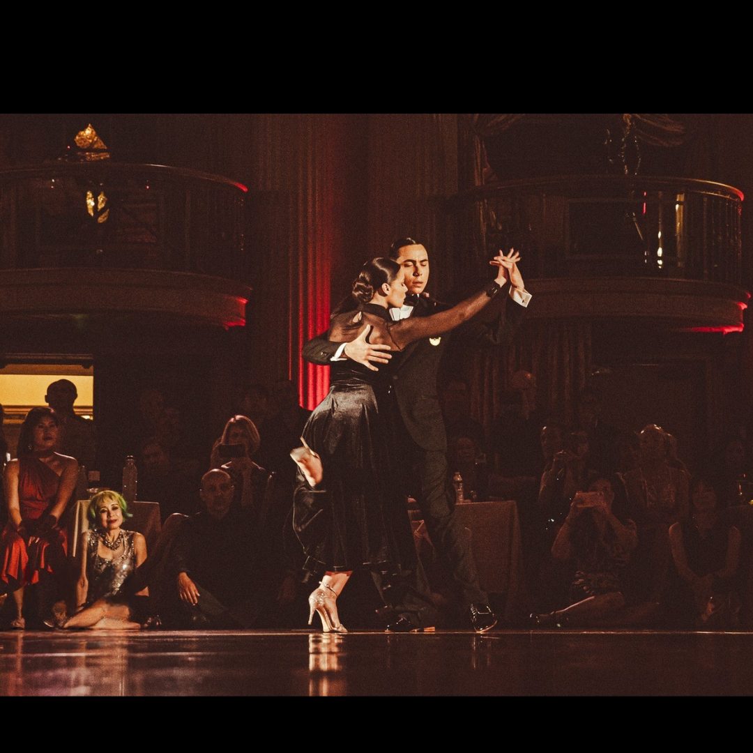A couple passionately dancing tango on stage with an engaged audience.