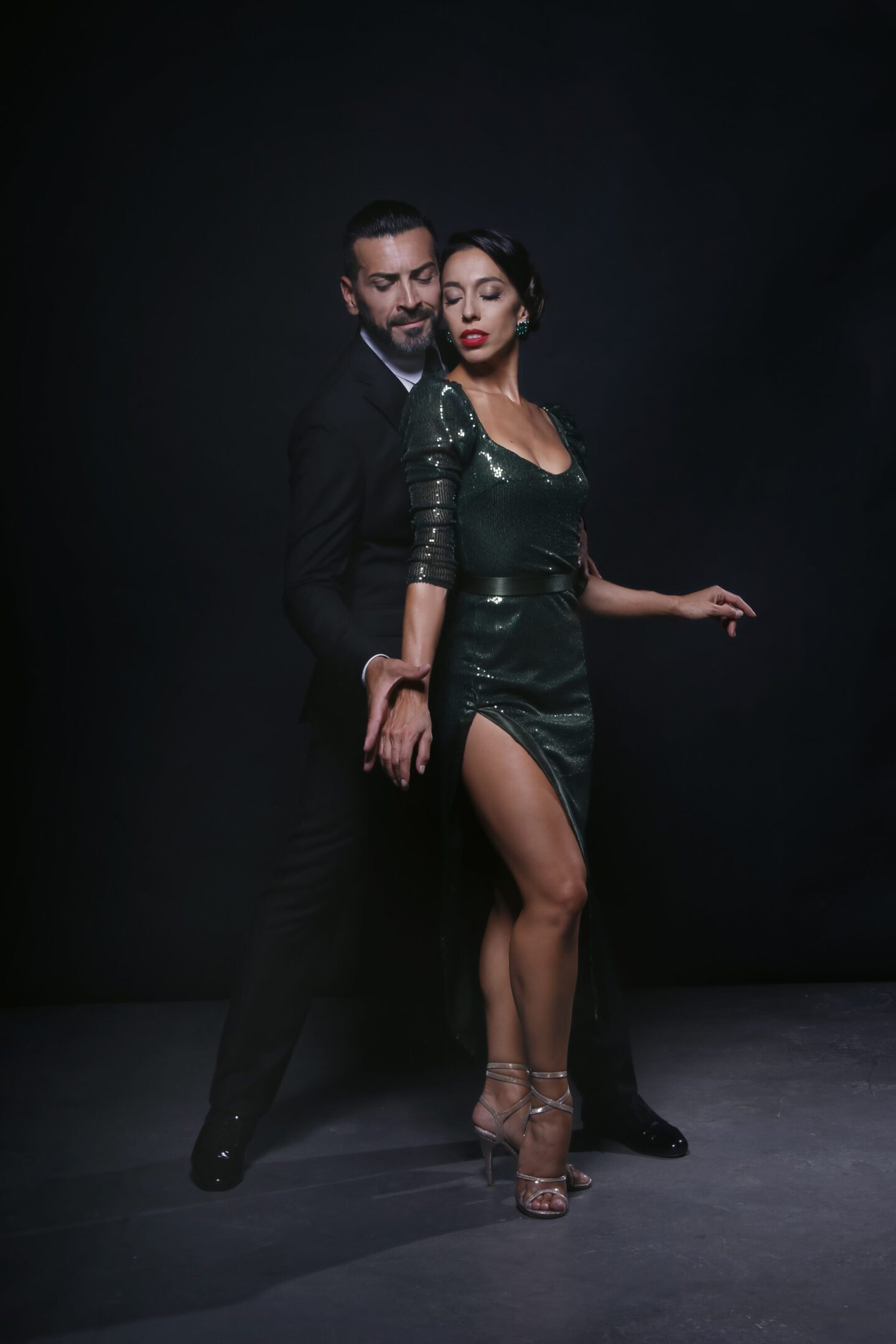 Elegant couple posing in stylish evening attire against a dark backdrop.